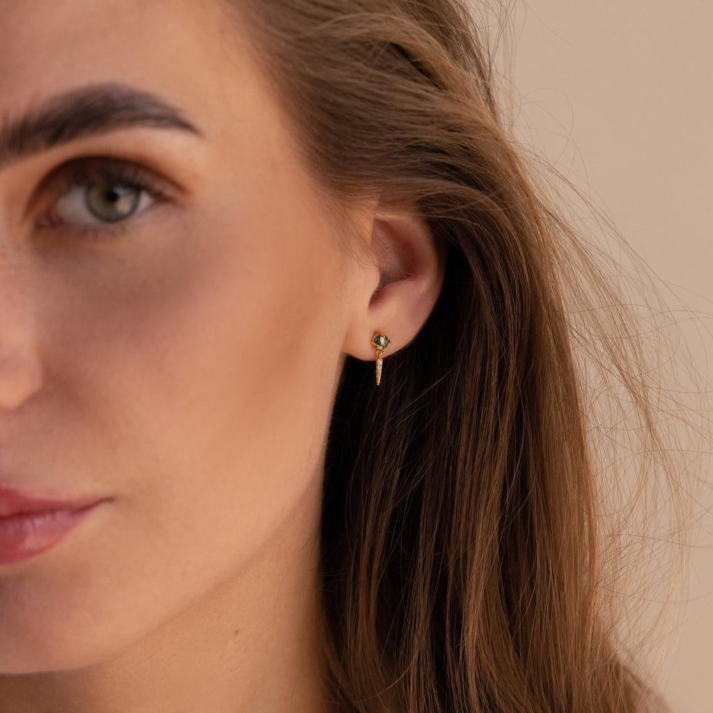 Close-up of a woman's face featuring elegant Agate Diamond Drop Earrings—small gold earrings adorned with green gemstones.