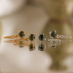 Two pairs of Agate Diamond Drop Earrings in gold and silver rest on a reflective surface, showcasing their striking dagger-shaped design.