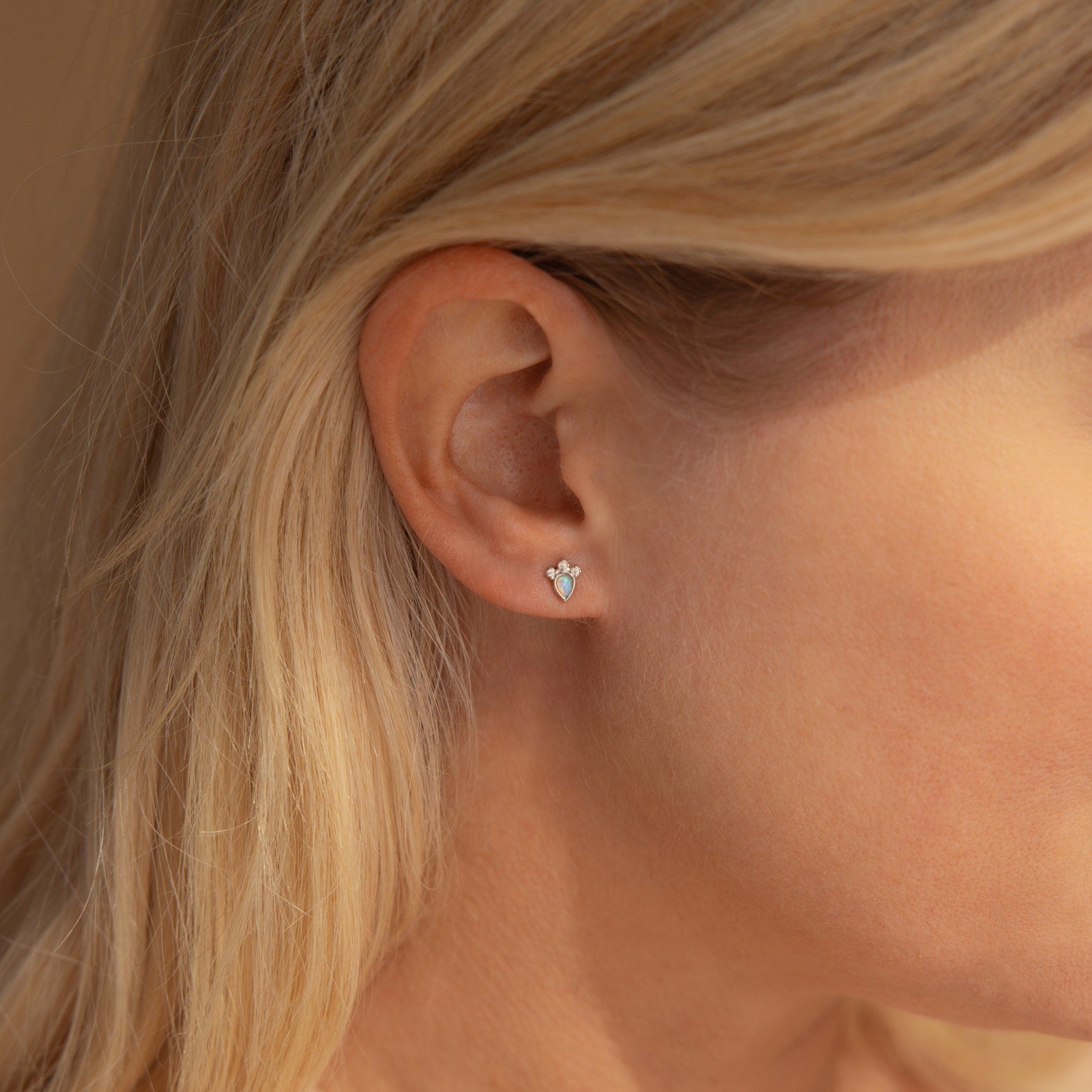 Close-up of a woman's ear wearing Dainty Opal Teardrop Studs, delicate earrings featuring shimmering opals in a subtle teardrop design.