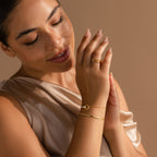 Woman with closed eyes wears a gold Interlocking Opal Inlay Bracelet and rings, posing gracefully against a beige background—an elegant showcase of minimalist jewelry.