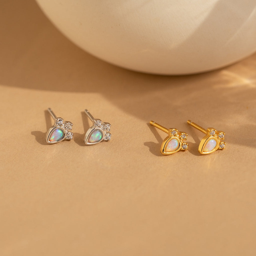 Dainty Opal Teardrop Studs: Two pairs, one silver and one gold, feature shimmering opal teardrops accented with tiny crystals. Elegant and versatile, these earrings offer a timeless sparkle inspired by classic diamond studs.