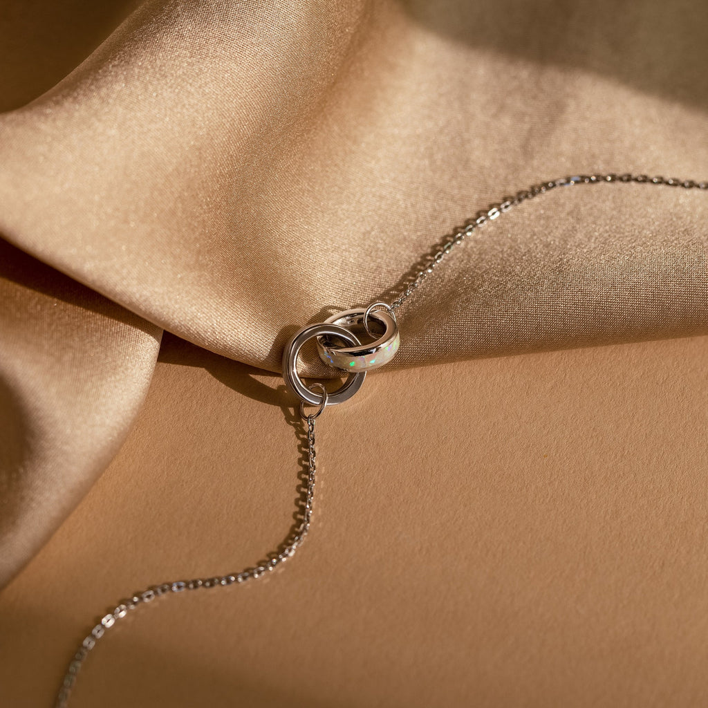 Interlocking Opal Inlay Necklace and Bracelet Set in Silver, inspired by interlocking rings, displayed on beige satin fabric under soft, warm lighting.