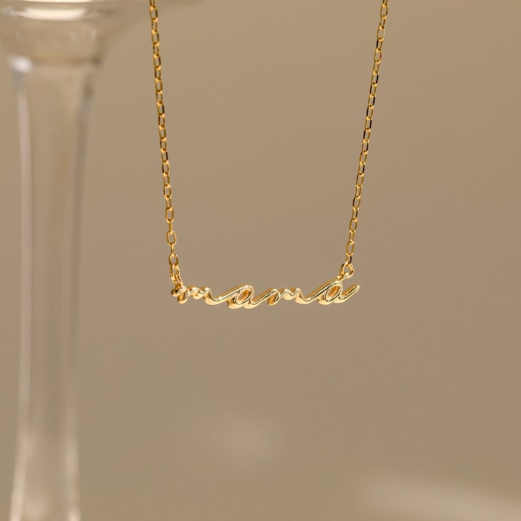 A Dainty Bubble Name Necklace featuring the word "mama" in gold bubble letters hangs against a neutral background, highlighting elegant personalized jewelry.