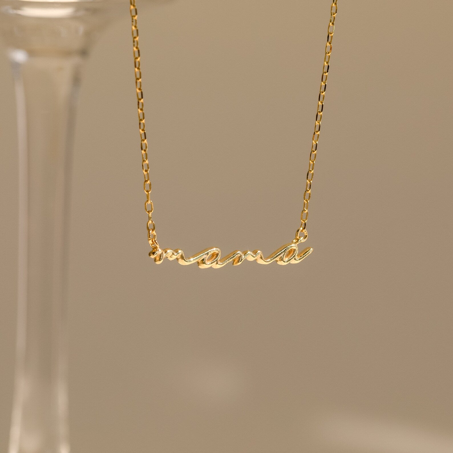 A Dainty Bubble Name Necklace featuring the word "mama" in gold bubble letters hangs against a neutral background, highlighting elegant personalized jewelry.