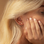 Close-up of a blonde woman wearing elegant Dainty Opal Teardrop Studs, with her hand partially covering her face.