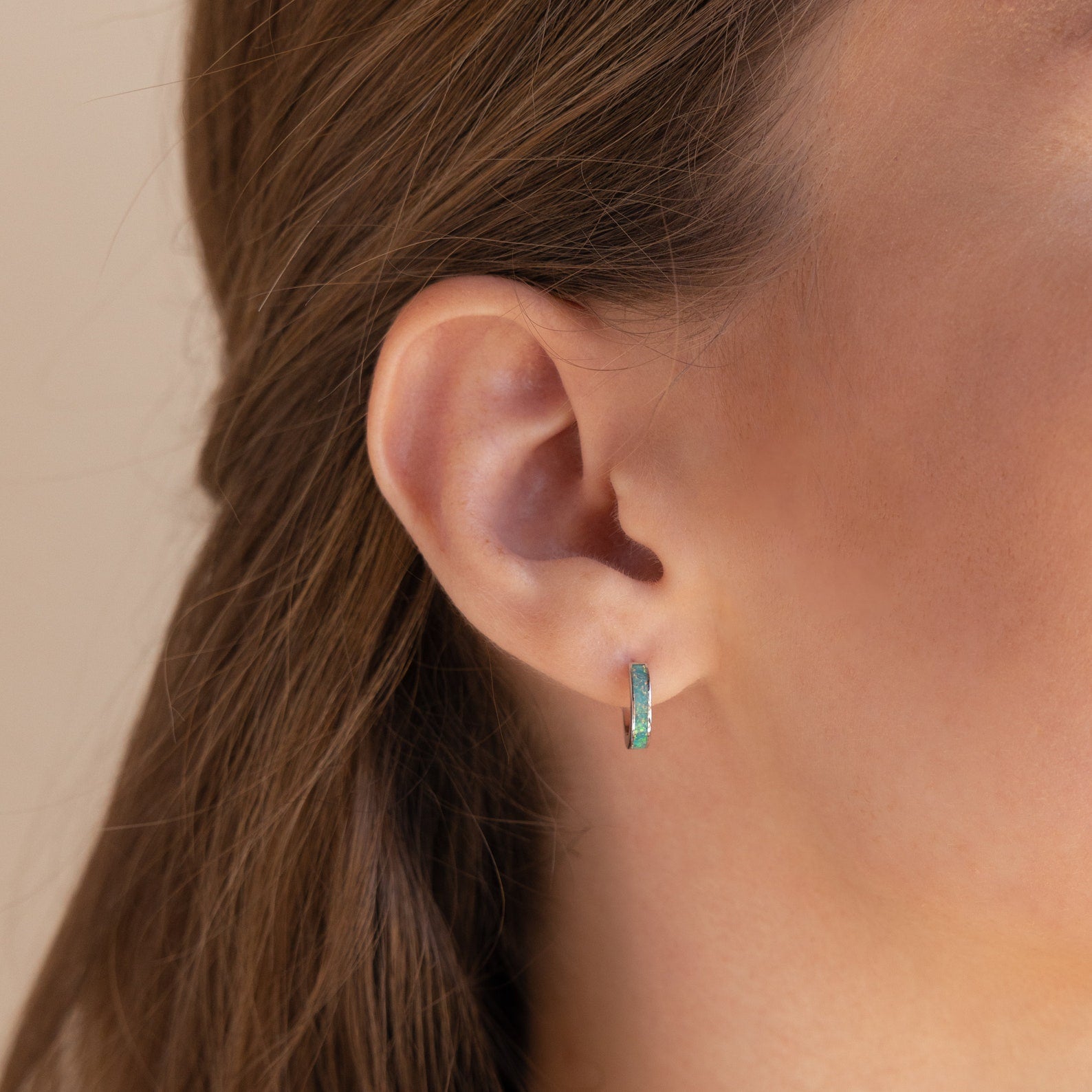 Close-up of a woman's ear wearing Green Opal Inlay Huggies, with brown hair tucked behind her ear.