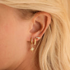 Close-up of a woman's ear with three gold earrings, including playful pieces—a dangling star and pearl charm—paired with Opal Marquise Studs for a touch of floral jewelry elegance.