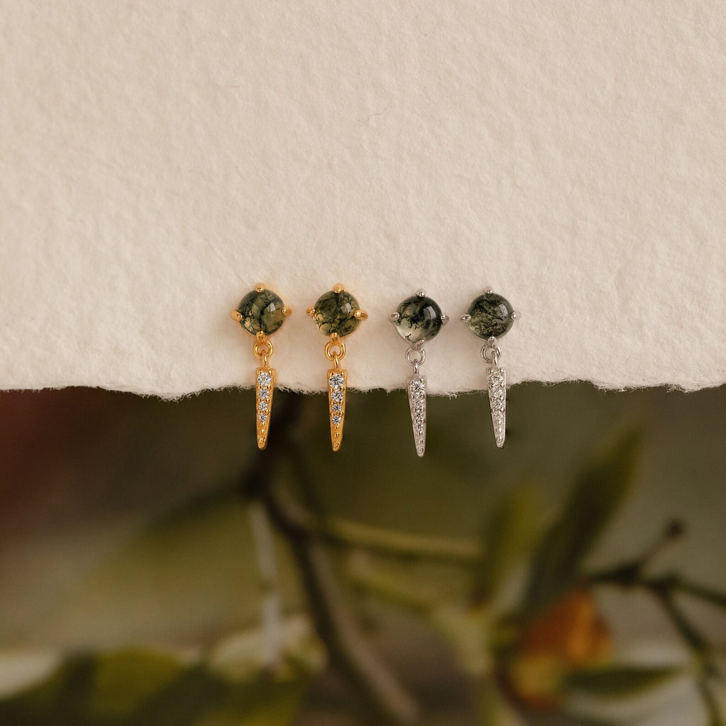Two pairs of Agate Diamond Drop Earrings—gemstone stud earrings with pointed dangles, one gold and one silver—are displayed on a textured surface.