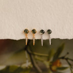 Two pairs of Agate Diamond Drop Earrings—gemstone stud earrings with pointed dangles, one gold and one silver—are displayed on a textured surface.