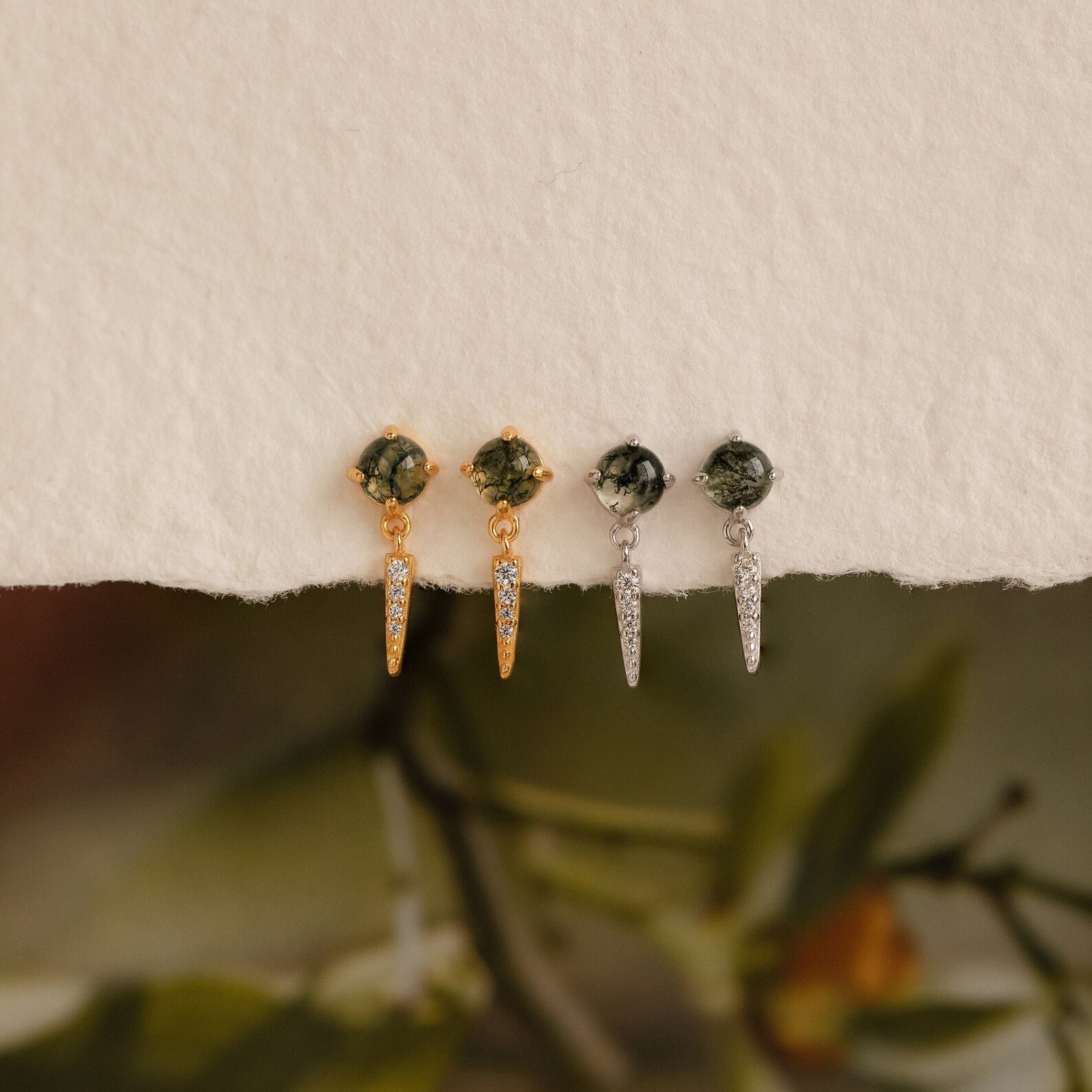 Two pairs of Agate Diamond Drop Earrings—gemstone stud earrings with pointed dangles, one gold and one silver—are displayed on a textured surface.