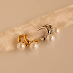 A pair each of gold and silver Pearl Drop Huggies resting on a plush, cream-colored fabric band