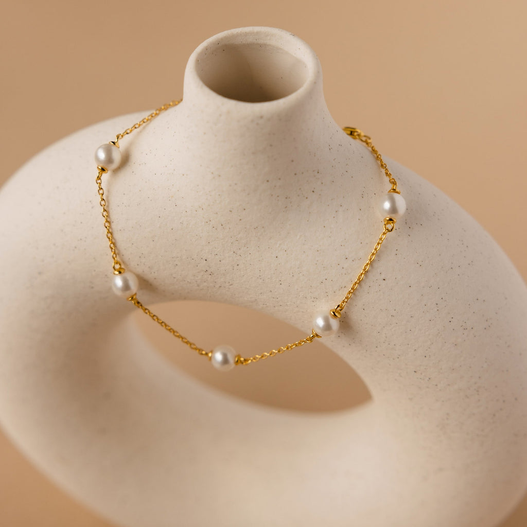 The Pearl Station Bracelet, featuring white pearls, is elegantly displayed draped over a cream abstract ceramic sculpture on a beige background, highlighting the modern sophistication of pearl jewelry.
