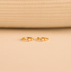 The gold huggies laid flat on a neutral surface, pearls and diamonds prominently featured in the design.