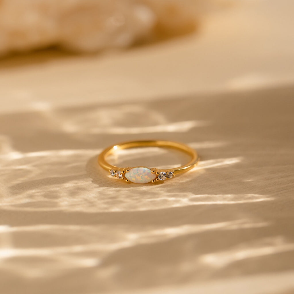 The Marquise Opal Diamond Ring features a central opal with sparkling diamond side stones, beautifully displayed on a textured, sunlit surface.