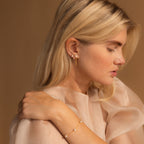 A woman wearing multiple earrings including the gold pearl diamond huggie as part of a stacked ear look, styled with a pearl bracelet.