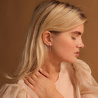 A woman with blonde hair and closed eyes wears Pearl Chain Studs earrings and a sheer beige blouse.