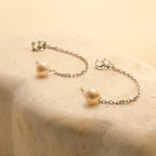 The Pearl Chain Studs, featuring elegant pearl drops, rest gracefully on a smooth beige stone surface.