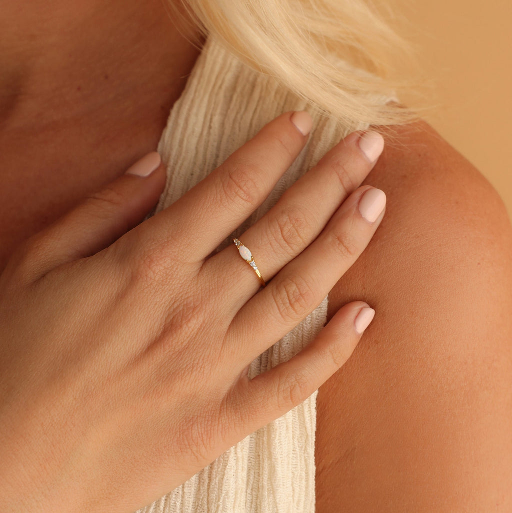 A hand with pale pink nails rests on a shoulder, adorned with the delicate Marquise Opal Diamond Ring set in gold.