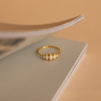 The Marquise Opal Statement Ring with white stones sits on the edge of an open book against a beige background, exuding vintage charm.