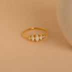 The Marquise Opal Statement Ring features four irregular white stones set in gold, radiating vintage charm, and is displayed on a beige surface next to a round white object.