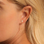 Close-up of a woman's ear wearing Pearl Chain Studs, featuring a pearl stud connected to a delicate gold chain hoop.
