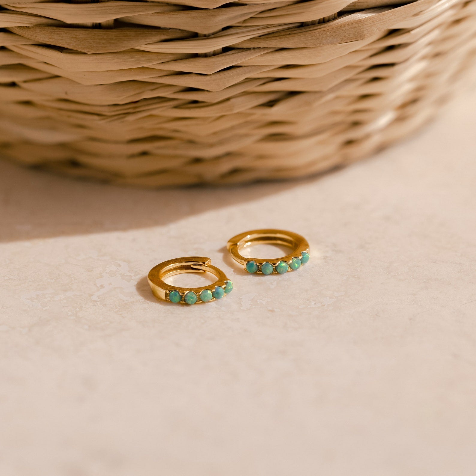 Garden Green Opal Huggies rest on a beige surface, ideal for stacking. A woven basket adds a natural touch in the background.