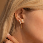 Close-up of a woman's ear adorned with dainty pearl studs and elegant Pearl Chain Studs, featuring small chains and delicate dangling details.