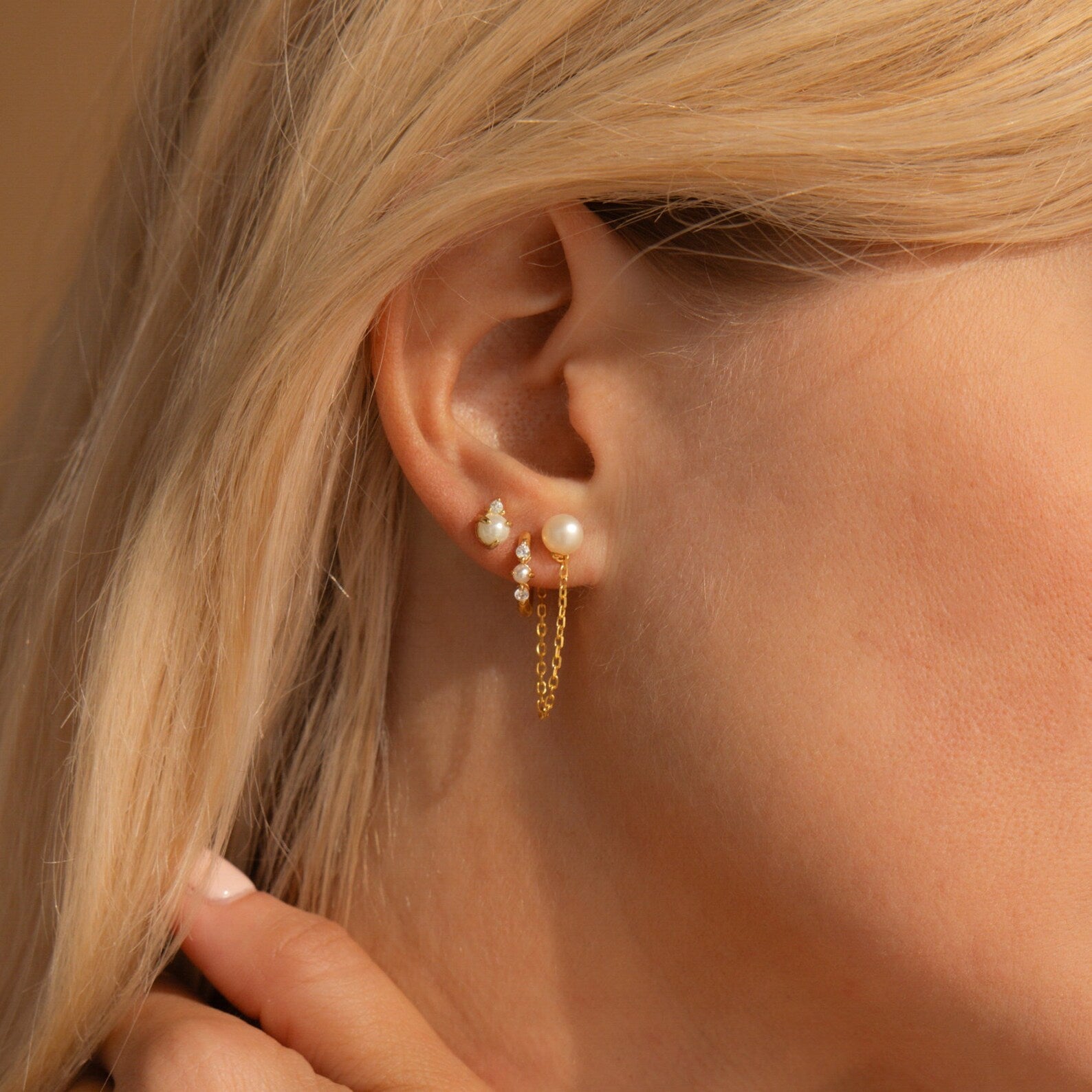 Close-up of a woman's ear adorned with dainty pearl studs and elegant Pearl Chain Studs, featuring small chains and delicate dangling details.