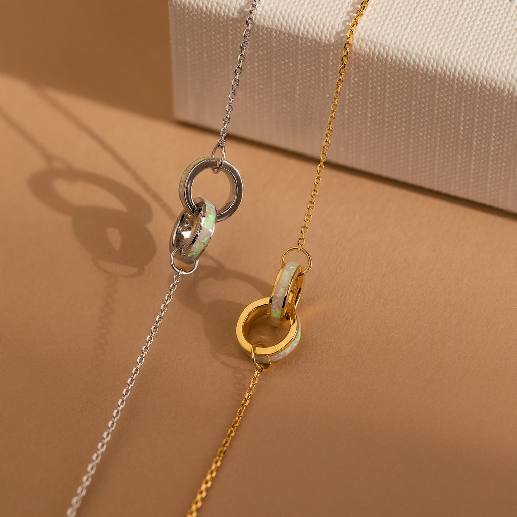 The Interlocking Opal Inlay Bracelet rests on a beige surface—its minimalist design makes it the perfect companion for your favorite necklaces or other dainty jewelry pieces.
