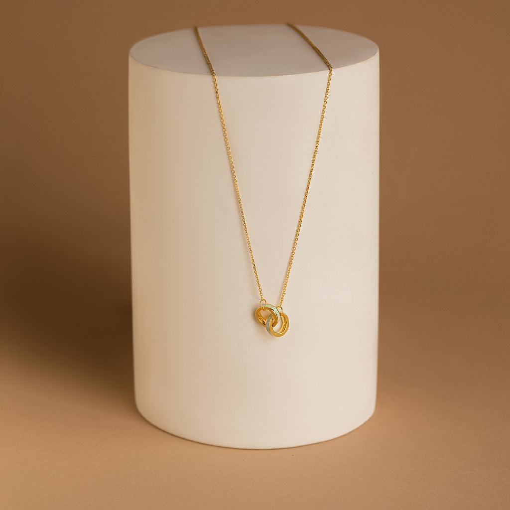 The Interlocking Opal Inlay Necklace and Bracelet Set in 18K Gold, displayed on a white cylindrical stand against a brown background, features interlocking rings and is perfect for pairing together.