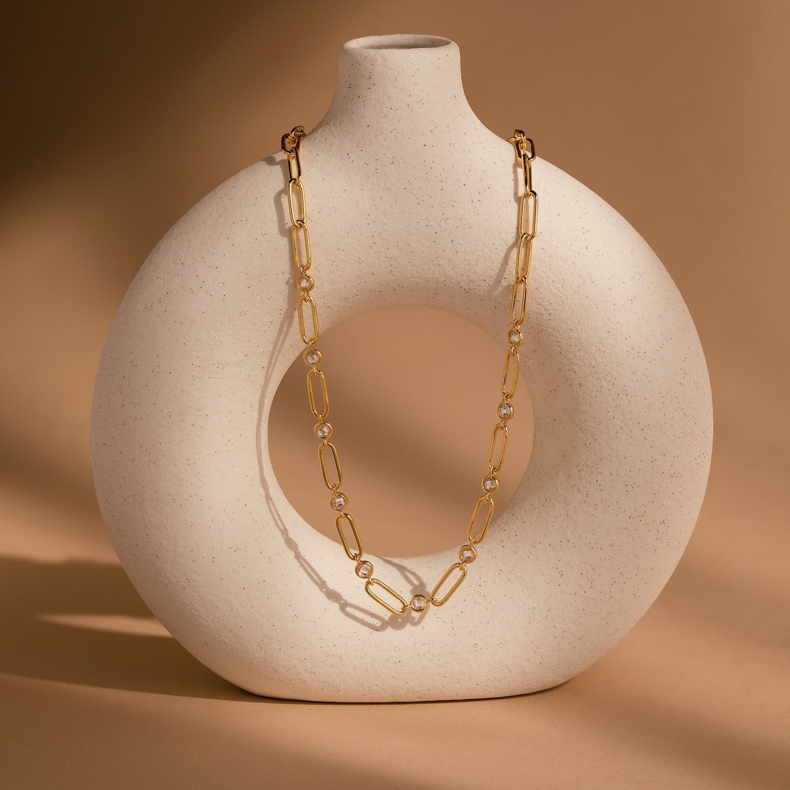 Diamond Paperclip Necklace with minimalist gold oval links draped over a round white ceramic vase on a beige background.
