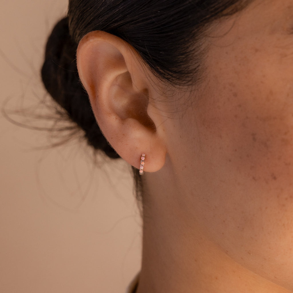 Close-up of a person’s ear with hair tied back, showcasing delicate Pink Opal Huggies—perfect for adding a feminine touch to any look.