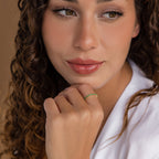 Woman with curly hair in a white top, resting her chin on her hand and wearing the Eternity Birthstone Ring—a delicate, customizable accessory that's the perfect Christmas gift.