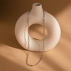 The Diamond Paperclip Necklace draped over a round, sculptural beige vase on a light brown background—a striking showcase of minimalist style and statement jewelry design.