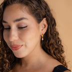A woman with curly hair wearing a black dress and Dangling Emerald Birthstone Hoops.