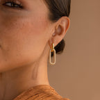 Close-up of a woman's ear wearing Pave Link Hoops—elegant gold earrings with diamond accents—set against a beige background.
