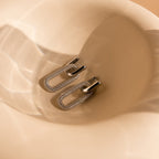 Pave Link Hoops rest on a soft beige, curved surface, catching the light with sparkling reflections from their silver and rhinestone design.