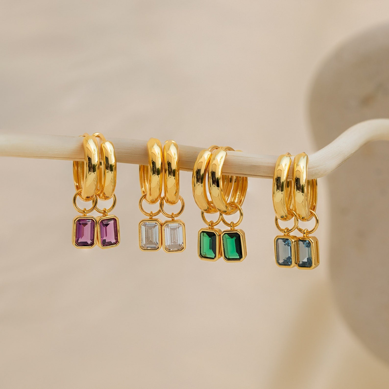 Four pairs of Dangling Emerald Birthstone Hoops with removable emerald-cut gemstones in purple, clear, green, and blue—perfect for a customizable birthstone look.