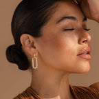 Woman with closed eyes wears Pave Link Hoops, her hair in a low bun and arm raised to her forehead.