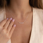 Close-up of a woman wearing the Tiny Dream Name Necklace with a personalized “maisie” pendant in cursive, paired with a light-colored blouse.