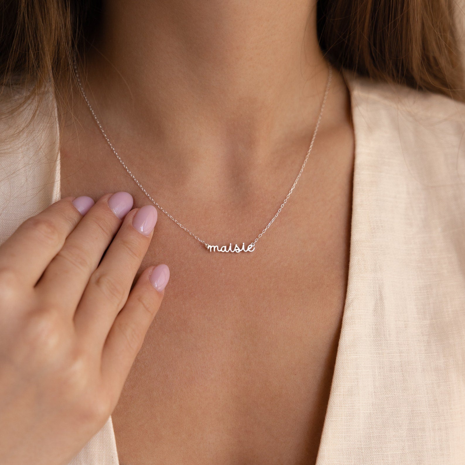 Close-up of a woman wearing the Tiny Dream Name Necklace with a personalized “maisie” pendant in cursive, paired with a light-colored blouse.