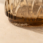 The Tiny Dream Name Necklace, featuring "Harper" in delicate cursive, rests at the base of a textured glass container.