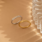 Two Dainty Mama Rings—one silver, one gold—with mama in script rest on a beige surface beside a clear textured glass object. They make perfect gifts for moms or anyone who loves delicate jewelry.