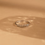 The Dainty Mama Ring, engraved with "mama," rests on a light brown surface with soft shadows—a minimalist and meaningful gift for any mother.
