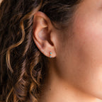 Close-up of a woman's ear with curly hair, wearing Emerald Birthstone Drop Studs—dainty earrings perfect for birth month jewelry lovers.