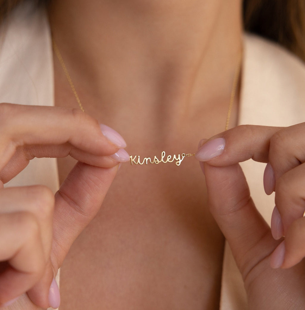 Close-up of hands holding a personalized Tiny Dream Name Necklace featuring the name Kinsley in elegant cursive letters.
