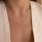 A person in a light-colored top wears a gold Tiny Dream Name Necklace featuring the name Kinsley in cursive font.