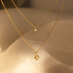 The Opal Star Duo Necklace—a gold double chain with a delicate opal and a sunburst charm—shines against a soft beige background.