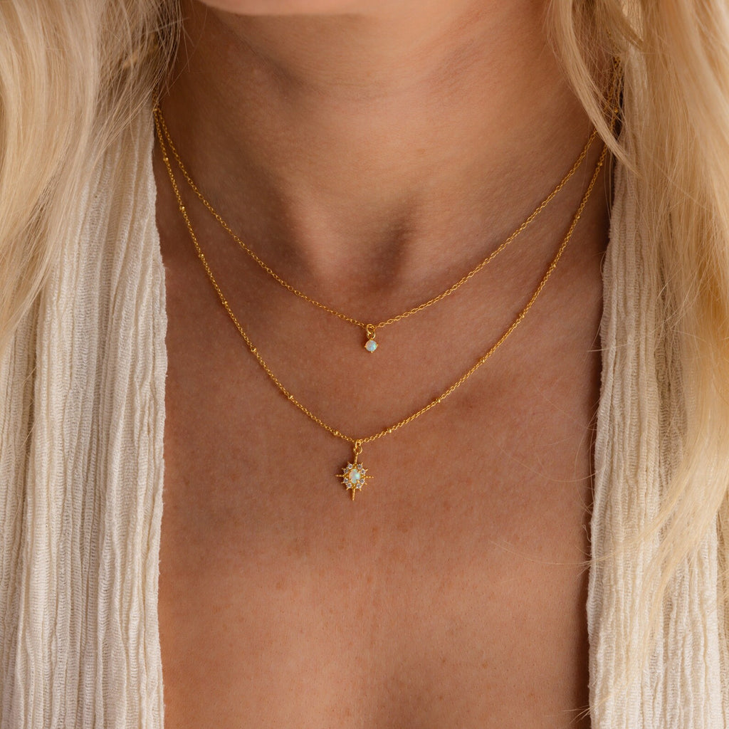 Close-up of a woman wearing the Opal Star Duo Necklace, a double chain featuring small jeweled pendants and an opal necklace with a subtle starburst design, against bare skin.