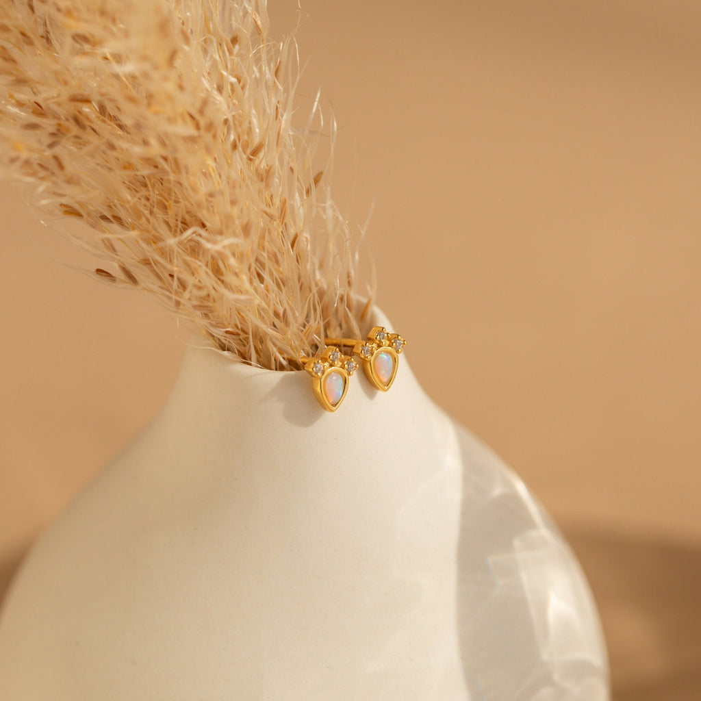 The Dainty Opal Teardrop Studs are displayed on a white vase with dried grass, set against a neutral background.